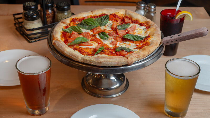 Pizza on serving tray with pints of beer