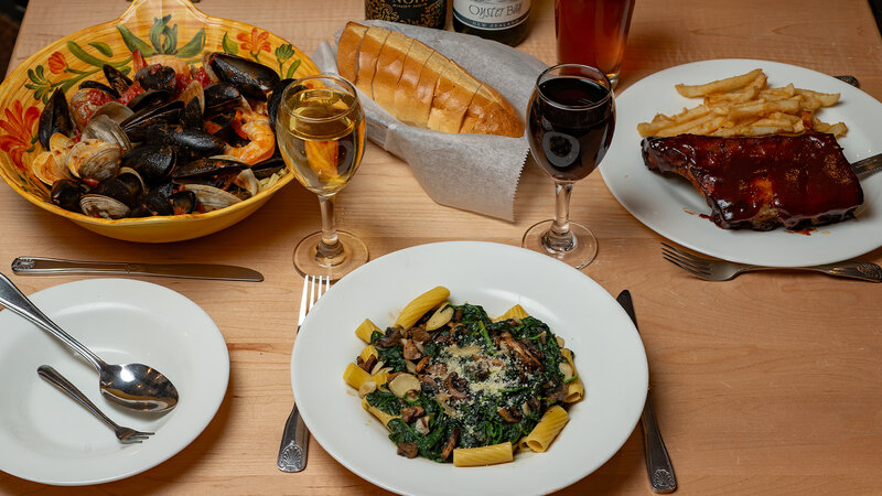 Multiple plated entrees with side of bread and two glasses of wine